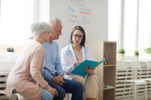 Portrait of young female doctor talking to senior couple while sitting in reception area of modern clinic, copy space